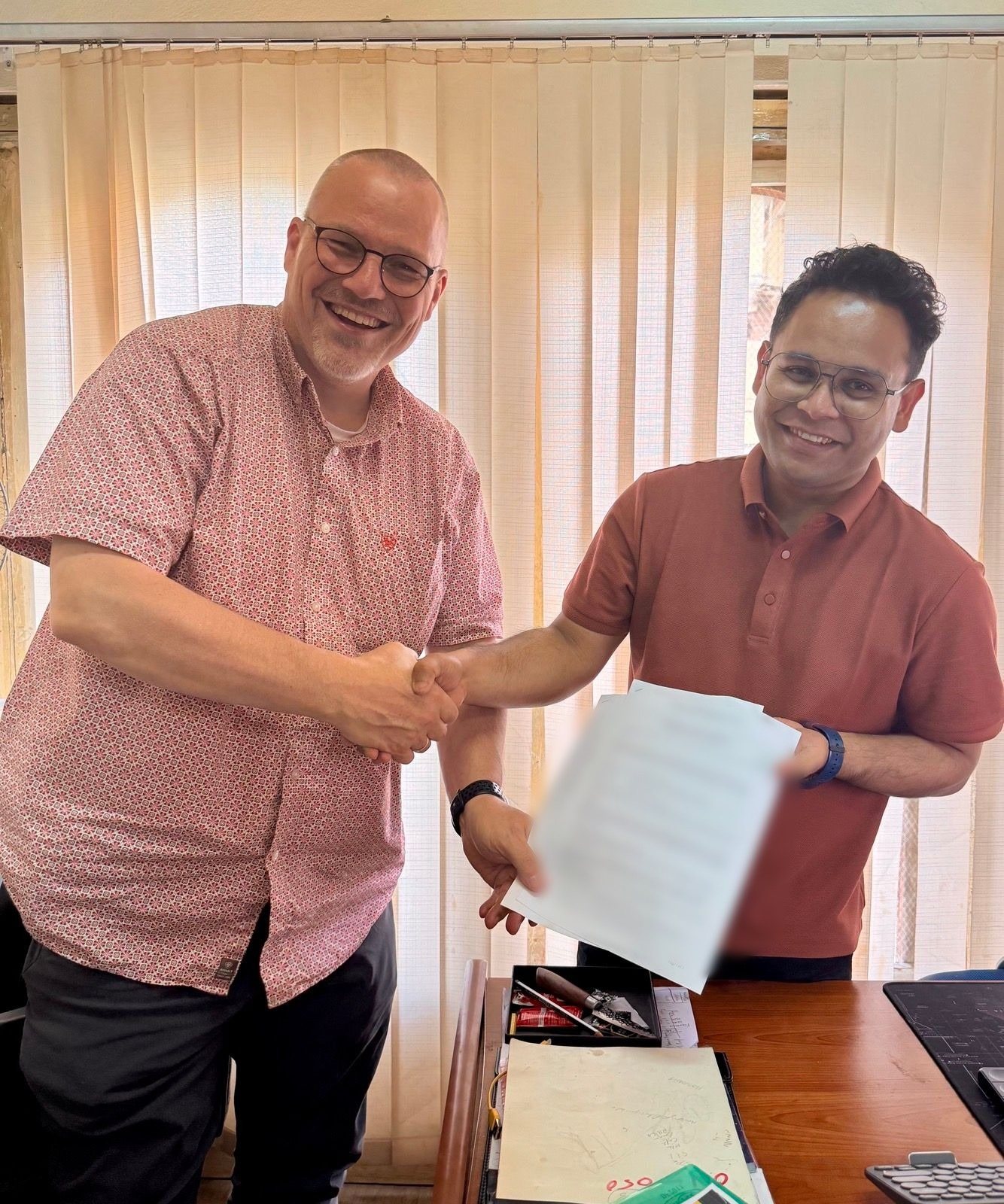 A Zampa director shaking hands with a new Bhutanese team member, holding his signed employment contract