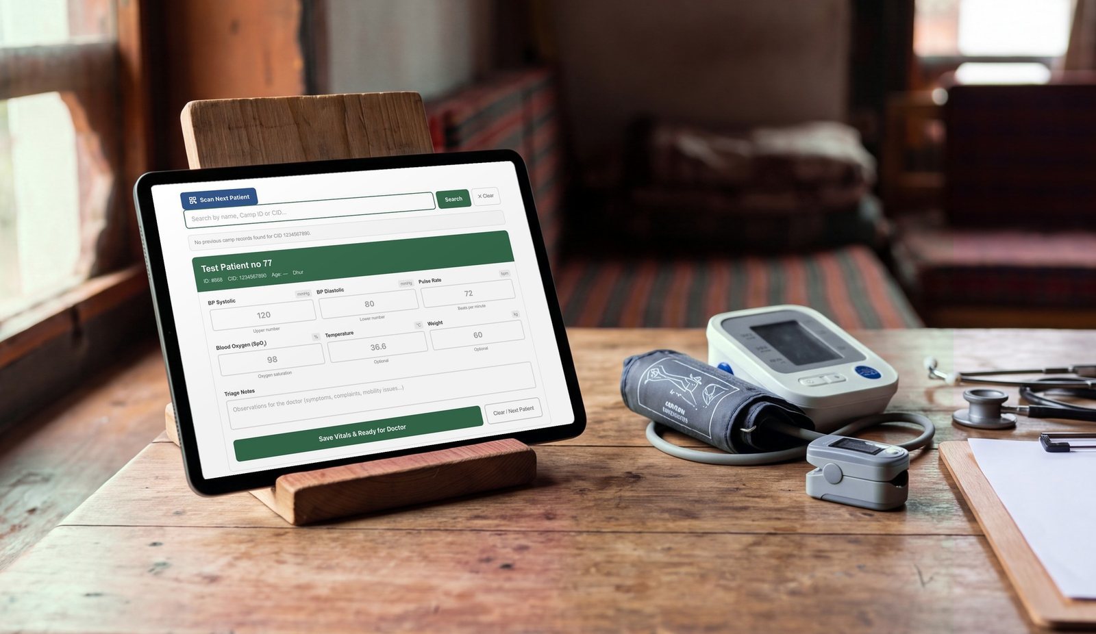 A tablet on a wooden desk showing a patient's triage form, beside a blood pressure monitor, a pulse oximeter and a stethoscope